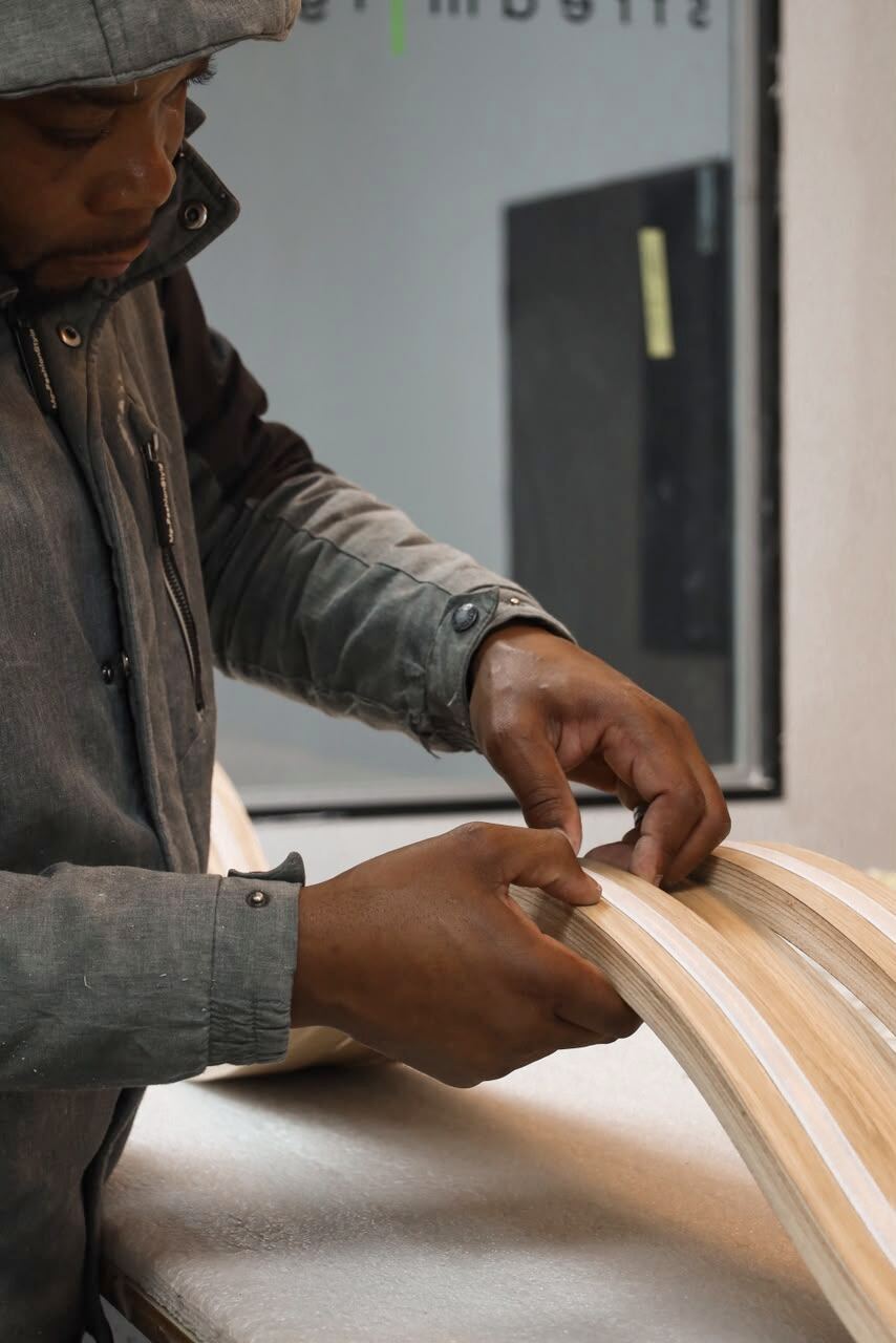 Hands checking the glue lines on a laminated curved timber light fixture
