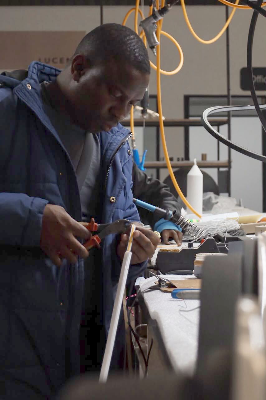 Technician assembling and soldering an LED strip fixture at the LUCENT assembly bench