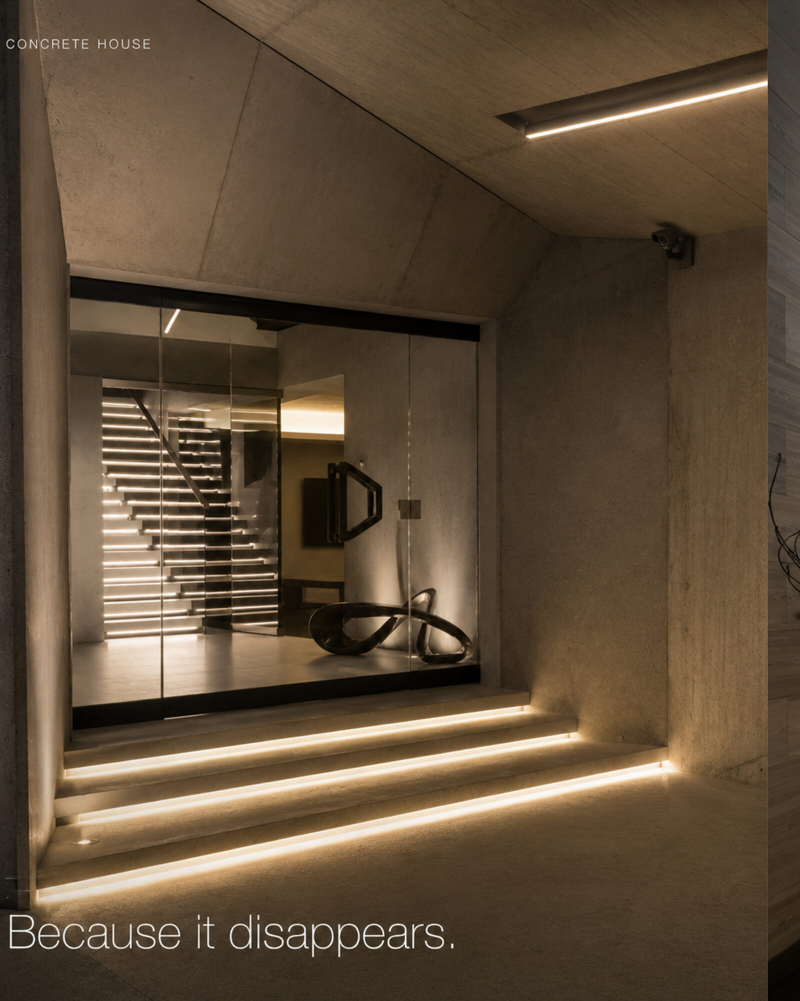Glass-fronted display of a modern concrete house entrance with integrated staircase lighting